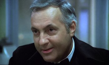 Movie still from “The Grilling” (1981), directed by Claude Miller – A person wearing a suit and tie; Close Up shot, Over the shoulder angle