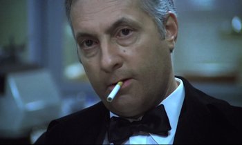 Movie still from “The Grilling” (1981), directed by Claude Miller – A person wearing a suit smoking a cigarette; Close Up shot, Low angle
