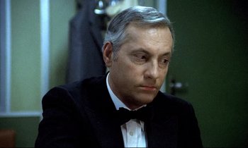 Movie still from “The Grilling” (1981), directed by Claude Miller – An older man in a suit and bow tie; Close Up shot, High angle