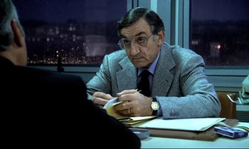 Movie still from “The Grilling” (1981), directed by Claude Miller – An older man sitting at a table writing on a piece of paper; Close Up shot, Over the shoulder angle