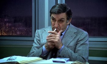 Movie still from “The Grilling” (1981), directed by Claude Miller – An older man sitting at a table with a cigarette in his mouth; Medium shot, High angle