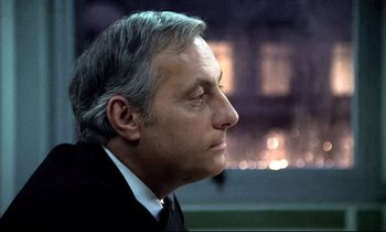 Movie still from “The Grilling” (1981), directed by Claude Miller – A person wearing a suit and tie; Close Up shot, Over the shoulder angle