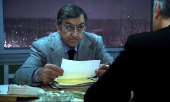 Movie still from “The Grilling” (1981), directed by Claude Miller – An older man sitting at a dinner table looking at a piece of paper; Close Up shot, Over the shoulder angle