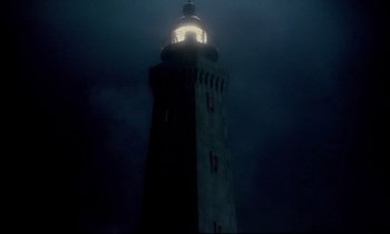 Movie still from “The Grilling” (1981), directed by Claude Miller – A light shining on the top of a light house at night; Extreme Wide shot, Low angle