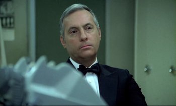 Movie still from “The Grilling” (1981), directed by Claude Miller – A person wearing a suit and bow tie; Close Up shot, Low angle