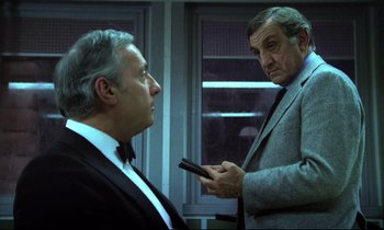 Movie still from “The Grilling” (1981), directed by Claude Miller – Two men in suits are looking at each other; Medium shot, Over the shoulder angle