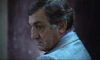 Movie still from “The Grilling” (1981), directed by Claude Miller – An older man wearing a suit and tie looking to his left; Close Up shot, Low angle