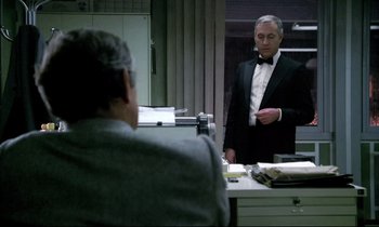 Movie still from “The Grilling” (1981), directed by Claude Miller – A man in a suit is looking at himself in the mirror; Medium shot, Over the shoulder angle