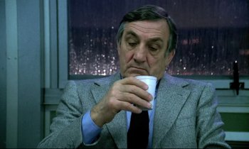 Movie still from “The Grilling” (1981), directed by Claude Miller – An older man wearing a suit and tie drinking a cup of coffee; Close Up shot, Low angle
