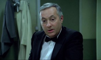 Movie still from “The Grilling” (1981), directed by Claude Miller – A person wearing a suit and a bow tie; Close Up shot, High angle