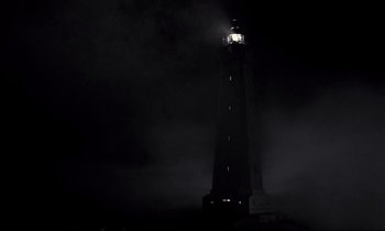 Movie still from “The Grilling” (1981), directed by Claude Miller – A light house is lit up at night with fog; Extreme Wide shot, Low angle