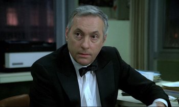 Movie still from “The Grilling” (1981), directed by Claude Miller – A person wearing a suit and a bow tie; Close Up shot, High angle