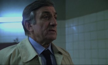 Movie still from “The Grilling” (1981), directed by Claude Miller – An older man wearing a trench coat and a tie; Close Up shot, Over the shoulder angle