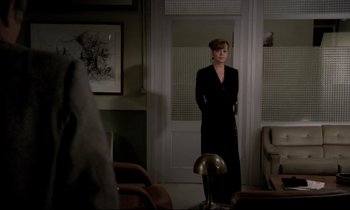 Movie still from “The Grilling” (1981), directed by Claude Miller – A woman in a black dress standing in front of a door; Wide shot, Over the shoulder angle