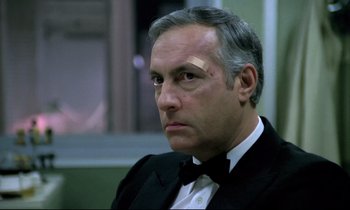 Movie still from “The Grilling” (1981), directed by Claude Miller – A person wearing a suit and a bow tie; Close Up shot, Low angle