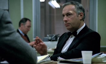 Movie still from “The Grilling” (1981), directed by Claude Miller – An older man in a suit sitting at a table; Close Up shot, Over the shoulder angle