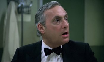 Movie still from “The Grilling” (1981), directed by Claude Miller – A man in a suit and bow tie looking up at the sky; Close Up shot, Low angle
