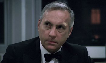Movie still from “The Grilling” (1981), directed by Claude Miller – An older man in a suit and bow tie; Close Up shot, Over the shoulder angle