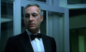Movie still from “The Grilling” (1981), directed by Claude Miller – A person wearing a suit and a bow tie; Close Up shot, Low angle