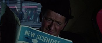 Movie still from “The Ipcress File” (1965), directed by Sidney J. Furie – A man in a black hat and a black tie looking at a magazine; Close Up shot, Over the shoulder angle