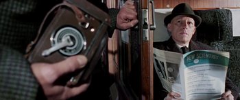 Movie still from “The Ipcress File” (1965), directed by Sidney J. Furie – A person holding a camera and a newspaper; Medium shot, Over the shoulder angle