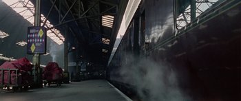 Movie still from “The Ipcress File” (1965), directed by Sidney J. Furie – A train traveling down train tracks next to a train station; Extreme Wide shot, High angle