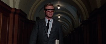 Movie still from “The Ipcress File” (1965), directed by Sidney J. Furie – A man in a suit and tie standing in a hallway; Medium shot, Low angle