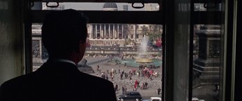 Movie still from “The Ipcress File” (1965), directed by Sidney J. Furie – A man in a suit looking out of a window at a fountain; Wide shot, High angle