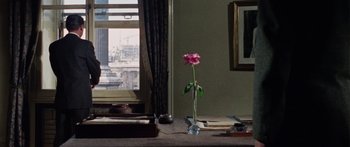 Movie still from “The Ipcress File” (1965), directed by Sidney J. Furie – A pink flower in a vase on a table in front of a window; Medium shot, High angle