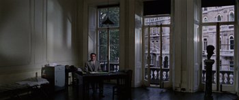 Movie still from “The Ipcress File” (1965), directed by Sidney J. Furie – A man sitting at a table in front of an open window; Wide shot, Low angle