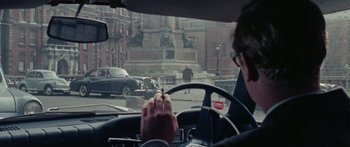 Movie still from “The Ipcress File” (1965), directed by Sidney J. Furie – A man driving a car in a city street; Wide shot, Over the shoulder angle