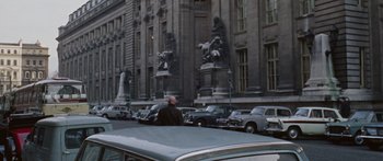 Movie still from “The Ipcress File” (1965), directed by Sidney J. Furie – A man sitting on the hood of a car in front of a building; Extreme Wide shot, High angle