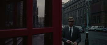 Movie still from “The Ipcress File” (1965), directed by Sidney J. Furie – A man standing in front of a red phone booth; Medium shot, Low angle
