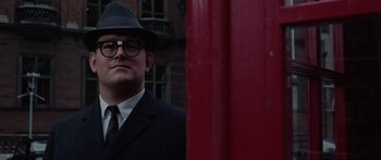 Movie still from “The Ipcress File” (1965), directed by Sidney J. Furie – A man in a suit and hat standing in front of a building; Close Up shot, Low angle