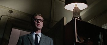 Movie still from “The Ipcress File” (1965), directed by Sidney J. Furie – A man in a suit and tie standing in front of a lamp; Close Up shot, Low angle