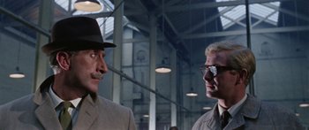 Movie still from “The Ipcress File” (1965), directed by Sidney J. Furie – Two men are standing next to each other in a building; Close Up shot, Low angle