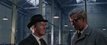 Movie still from “The Ipcress File” (1965), directed by Sidney J. Furie – A man in a suit and hat talking to another man in a suit and hat; Close Up shot, Over the shoulder angle