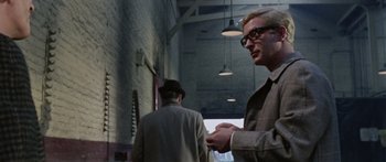 Movie still from “The Ipcress File” (1965), directed by Sidney J. Furie – A man in a suit and hat standing next to another man in a hat; Medium shot, Over the shoulder angle
