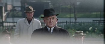 Movie still from “The Ipcress File” (1965), directed by Sidney J. Furie – An older man wearing a black hat and a suit; Close Up shot, Over the shoulder angle