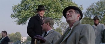 Movie still from “The Ipcress File” (1965), directed by Sidney J. Furie – A group of men standing next to each other in a park; Close Up shot, Low angle