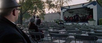 Movie still from “The Ipcress File” (1965), directed by Sidney J. Furie – A group of people sitting on folding chairs in front of an outdoor stage; Extreme Wide shot, High angle