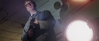 Movie still from “The Ipcress File” (1965), directed by Sidney J. Furie – A man holding a gun while standing next to an object; Medium shot, Low angle