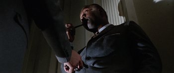 Movie still from “The Ipcress File” (1965), directed by Sidney J. Furie – A man in a gray suit is holding a pipe in his mouth; Close Up shot, Low angle