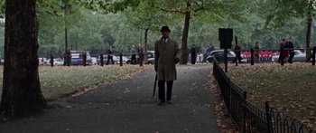 Movie still from “The Ipcress File” (1965), directed by Sidney J. Furie – A man in a hat and coat holding an umbrella on a sidewalk; Wide shot, High angle