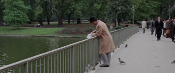 Movie still from “The Ipcress File” (1965), directed by Sidney J. Furie – An older man in a hat and coat standing on a bridge near a bird; Wide shot, High angle