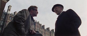 Movie still from “The Ipcress File” (1965), directed by Sidney J. Furie – Two men talking to each other in front of a building; Medium shot, Low angle