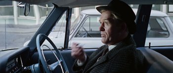 Movie still from “The Ipcress File” (1965), directed by Sidney J. Furie – An older man in a hat driving a car; Medium shot, Over the shoulder angle