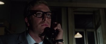Movie still from “The Ipcress File” (1965), directed by Sidney J. Furie – A man in a suit and glasses talking on a phone; Close Up shot, Low angle