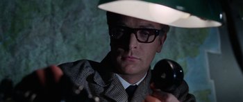 Movie still from “The Ipcress File” (1965), directed by Sidney J. Furie – A man in a hat and glasses holding a camera; Close Up shot, Low angle