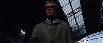 Movie still from “The Ipcress File” (1965), directed by Sidney J. Furie – A man in a suit and tie standing in a dark room; Close Up shot, Low angle